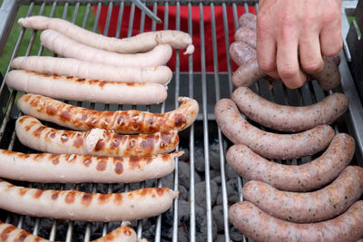 Cropped image of hand cooking sausages on barbeque grill