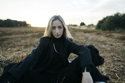 Portrait of young woman sitting on field against sky