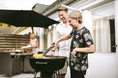 Son preparing barbecue meal with father in back yard