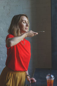 Woman holding cigarette while standing against wall