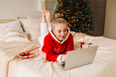 Smiling young woman using laptop on bed