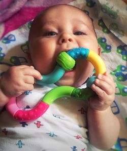 High angle portrait of baby girl holding toy while lying on bed at home