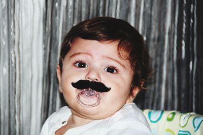 Close-up portrait of boy with mustache prop on pacifier