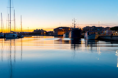 Sailboats moored at harbor against sky during sunset