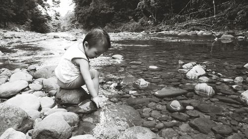 Cute toddler girl sitting on rock by stream at forest