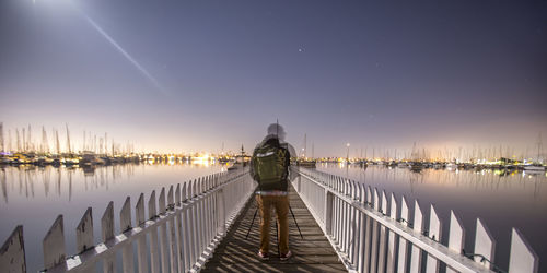 Rear view of man standing on pier at lake against sky