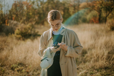 A young woman using her phone in a field during a sunny autumn day