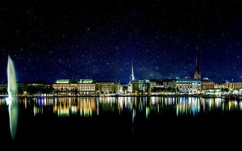 Illuminated buildings by lake against sky in city at night