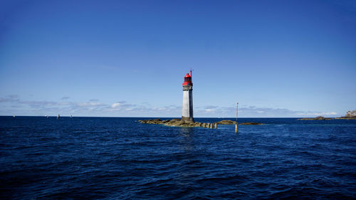 Lighthouse by sea against blue sky