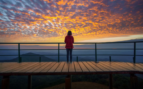 Rear view of woman looking at swimming pool against sky during sunset