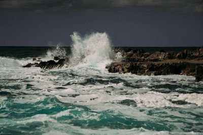 Waves splashing on rocks against clear sky