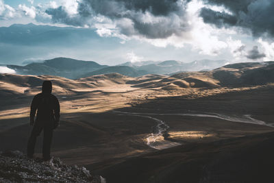 Rear view of man standing on mountain against sky