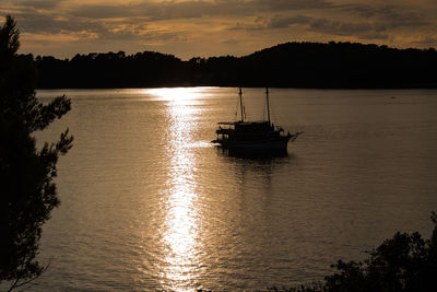 Silhouette boat sailing on river against sky during sunset