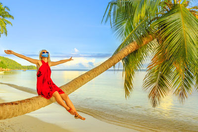 Woman standing by palm tree on beach against sky