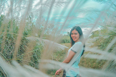 Side view portrait of smiling young woman standing by plants on land