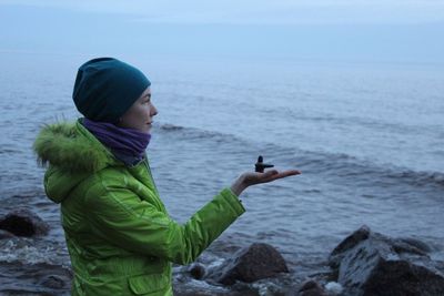 Side view of woman holding shiv ling while standing against sea