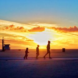 Silhouette people on beach against sky during sunset