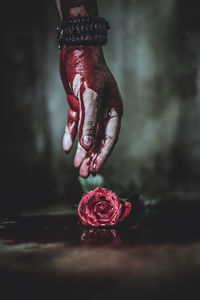 Cropped hand of person with blood reaching to rose on floor