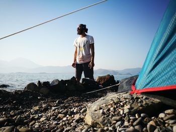 Man standing on rock by sea against sky