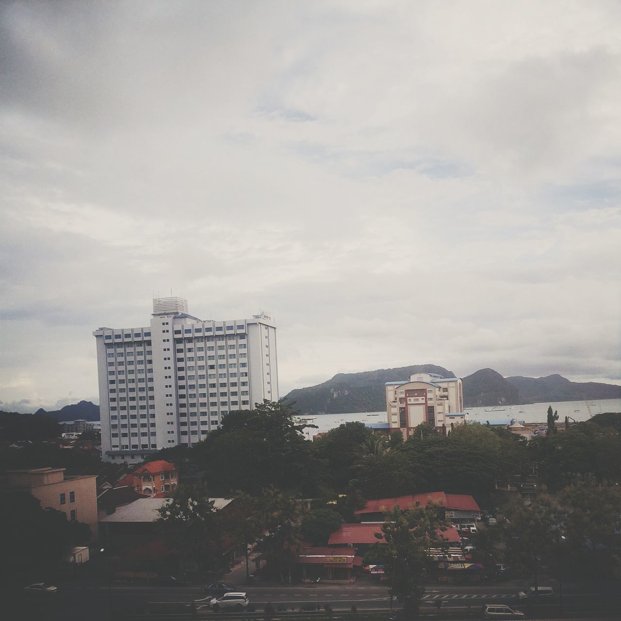 building exterior, architecture, built structure, sky, city, cloud - sky, cloudy, tree, residential building, building, street, road, residential structure, car, cloud, cityscape, residential district, outdoors, day, city life