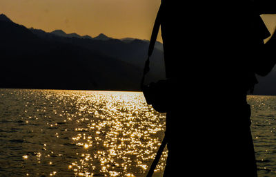 Silhouette of man standing by sea against sky during sunset