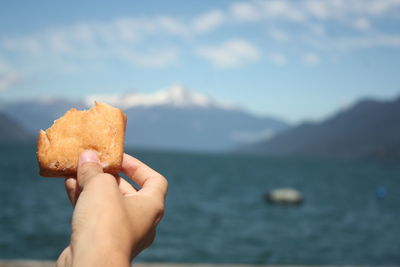 Cropped hand holding food against sea