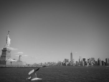 Bird flying over hudson river by statue of liberty against sky in city