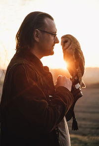 Man and wild bird over sunset sky in field looking on each other owl symbol of power, wisdom wealth
