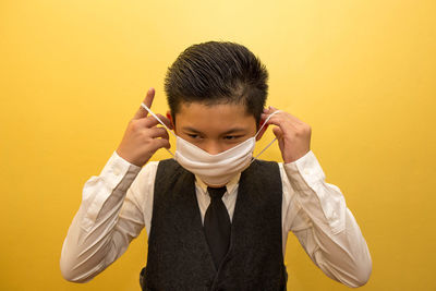 Boy wearing mask standing against yellow wall