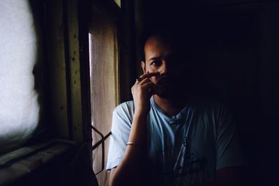 Portrait of young man sitting at home by window