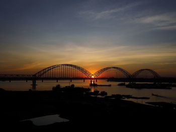 Silhouette bridge over river against sky during sunset