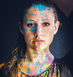 Close-up portrait of serious young woman face covered with colorful powder paint