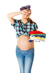 Tired pregnant woman holding clothes while standing against white background
