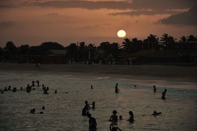 Group of people by sea against sky during sunset