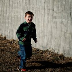 Smiling boy running on field by wall