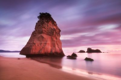 Rock formation in sea against sky during sunset