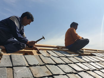 Men sitting on roof against sky