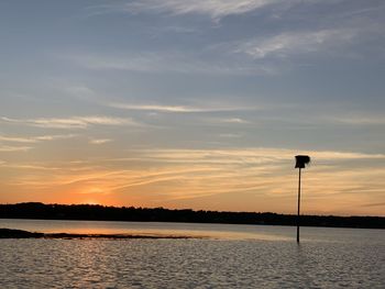 Silhouette street by lake against sky during sunset