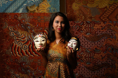 Portrait of smiling young woman holding mask against wall