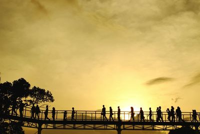 Silhouette people walking on footbridge against orange sky