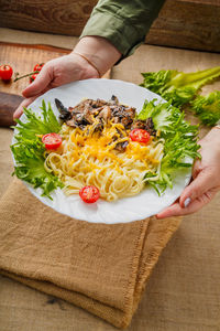 A plate of pasta with mushrooms and cheese decorated with herbs in female hands. vertical photo