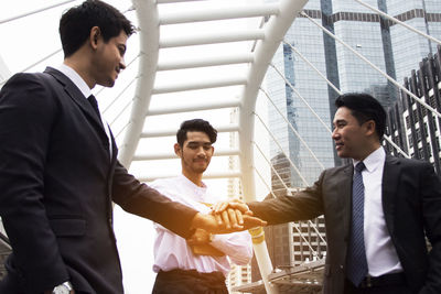 Businessmen stacking hands while standing in city