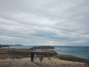 Rear view of people on land by sea against sky