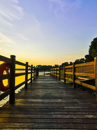 Empty footpath leading towards bridge against sky during sunset