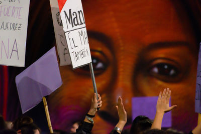 Cropped hands of person holding billboard with text by people during protest