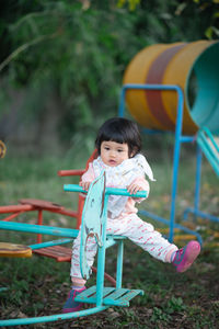 Cute girl looking away while sitting on equipment in playground