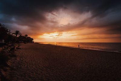 Scenic view of beach against cloudy sky during sunset