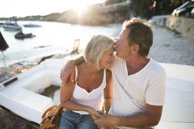 Senior couple sitting on edge of a boat on the beach at evening twilight