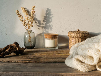 Autumn home still life of dry flowers, straw box, candle, knitted blanket on rustic wooden table 
