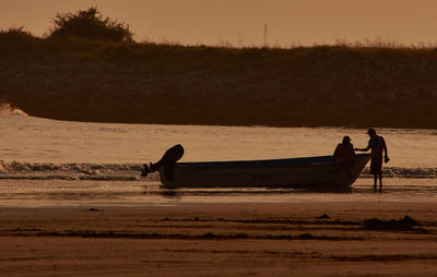 Friends with motor boat at beach against sky during sunset